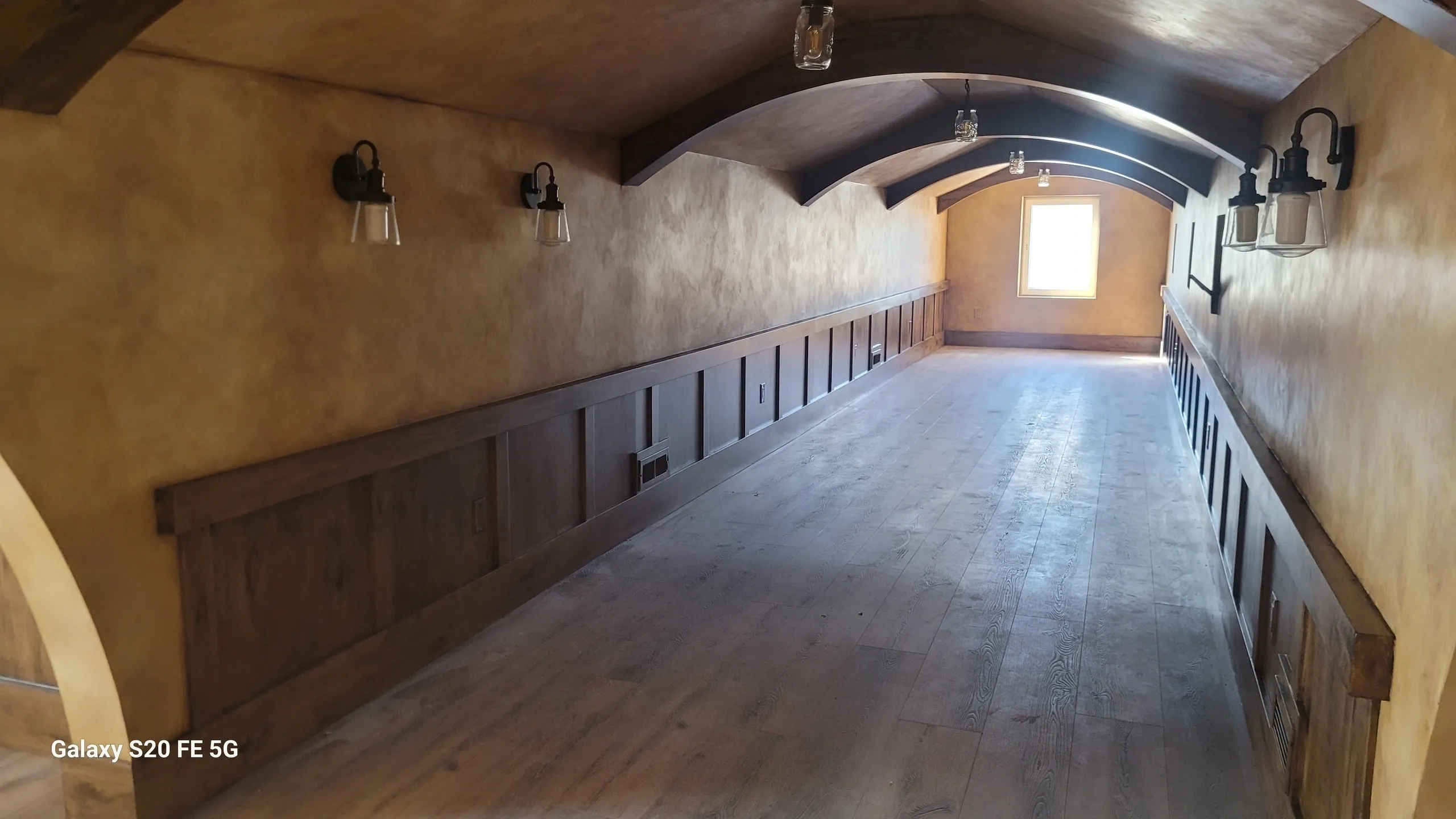 Wooden hallway with arched ceiling and lights.