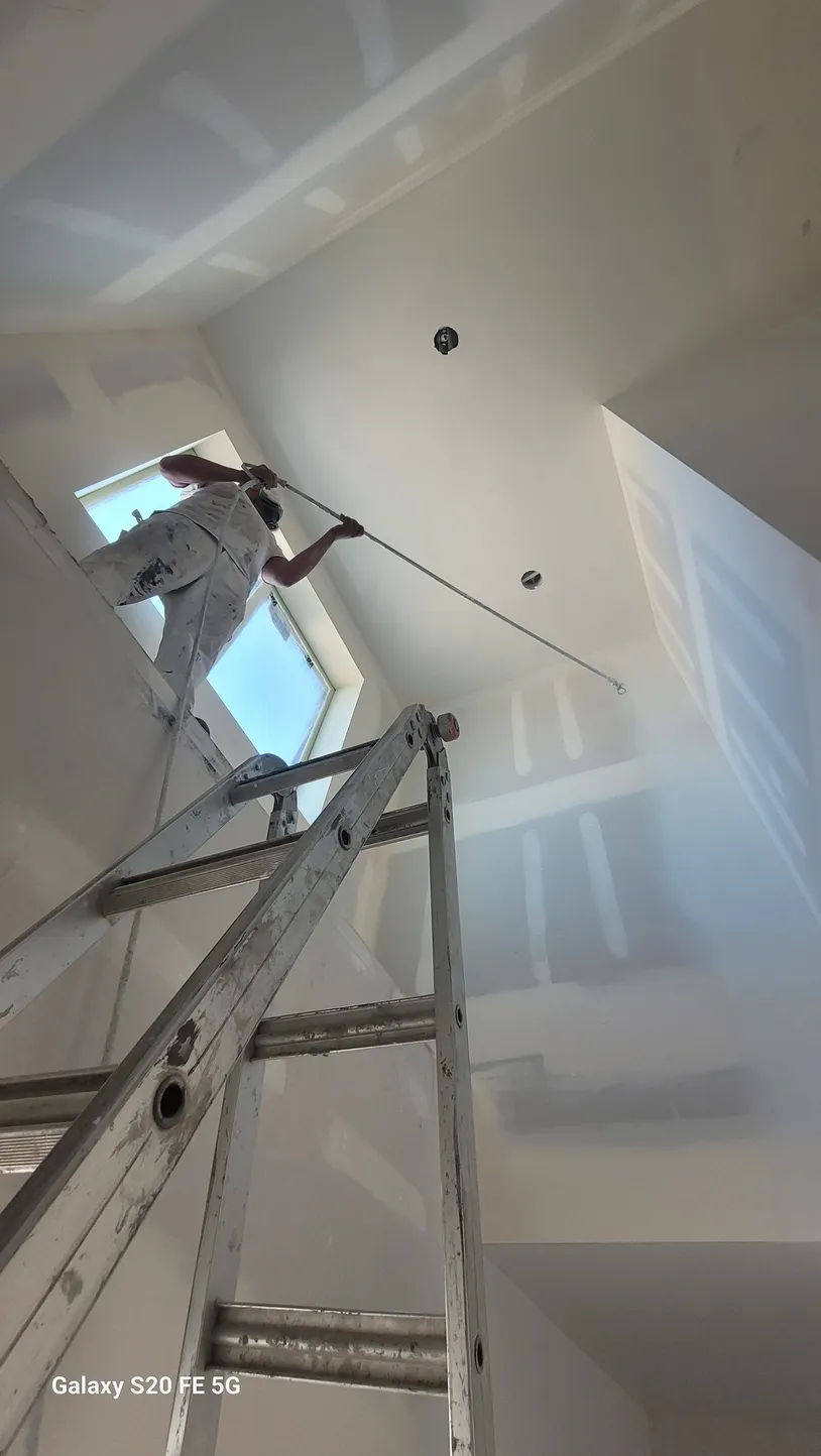 Person painting ceiling near a window.